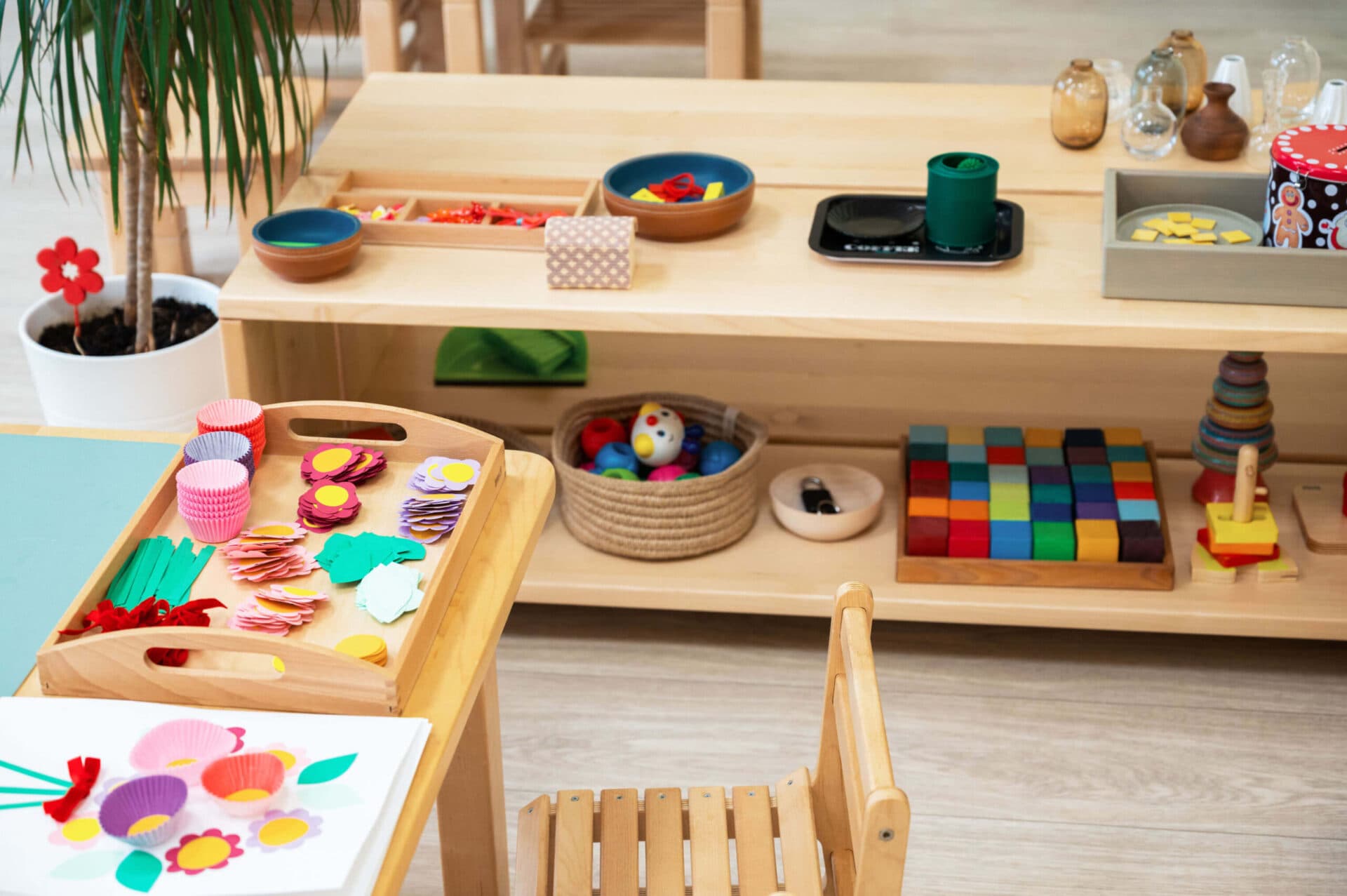 Wooden classroom shelves with colorful blocks, stacking toys, and a tray of craft materials