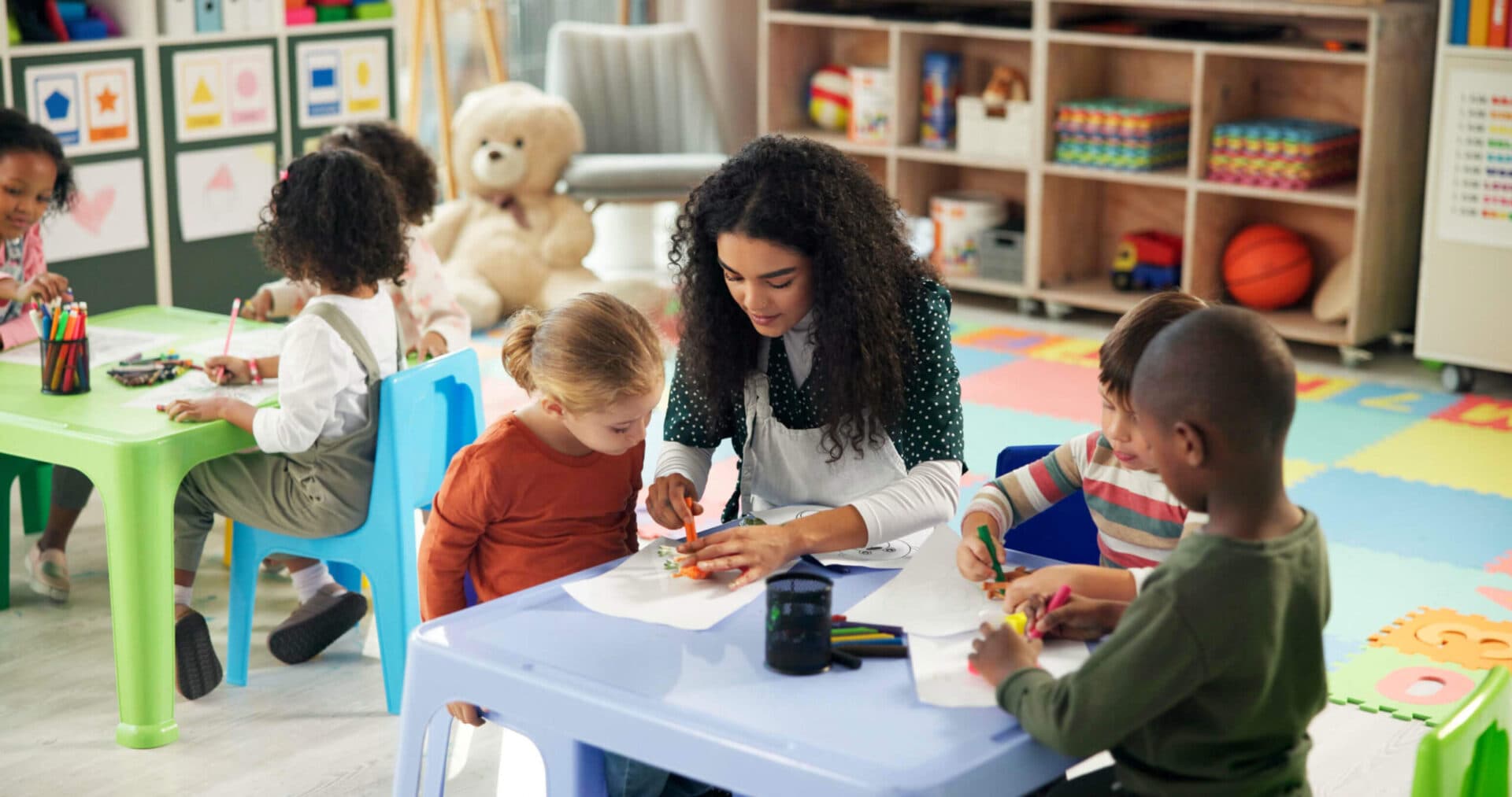 A teacher coloring with a small group of preschoolers at a classroom table
