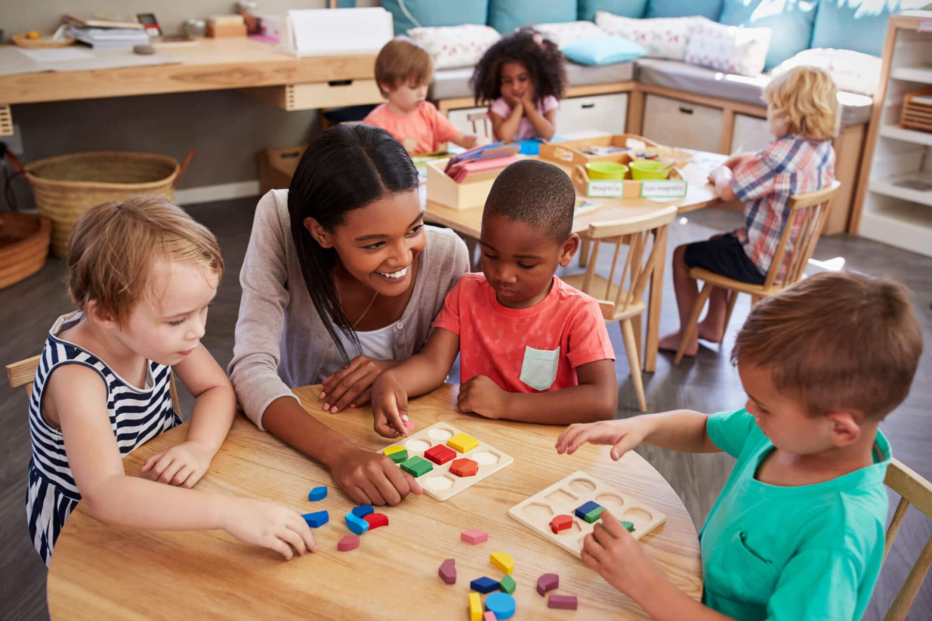 A smiling teacher helping children with wooden shape puzzles